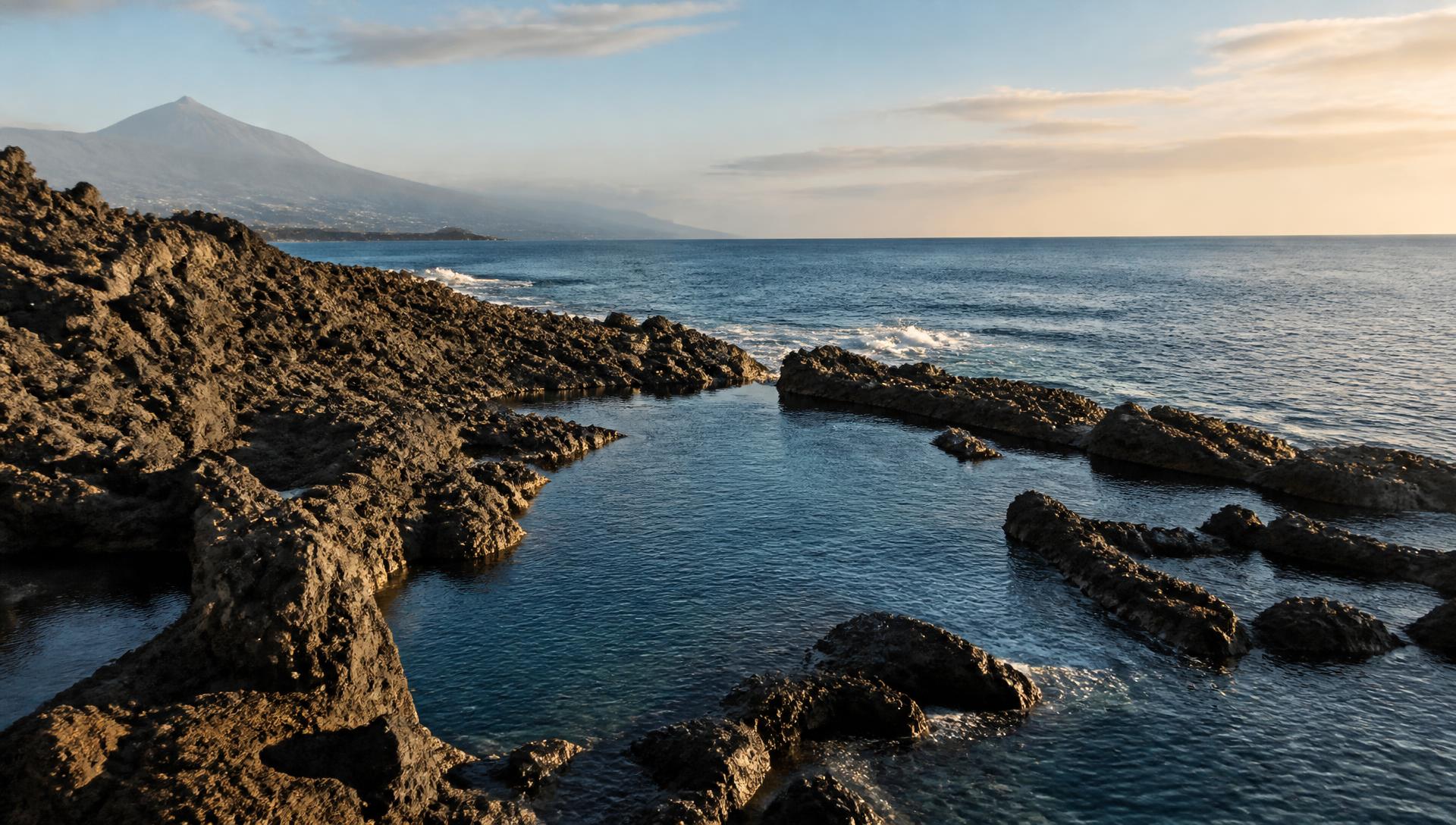 Volcanic coastline in Tenerife at golden hour with a natural sea pool and Mount Teide in the distance