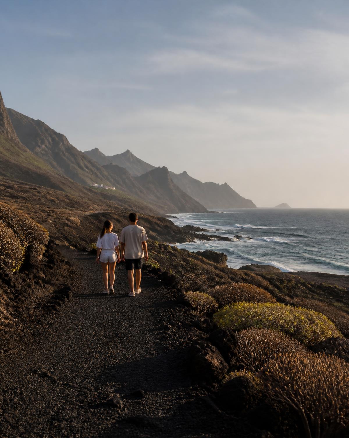 A couple walking a black volcanic coastal path in Tenerife in warm evening light