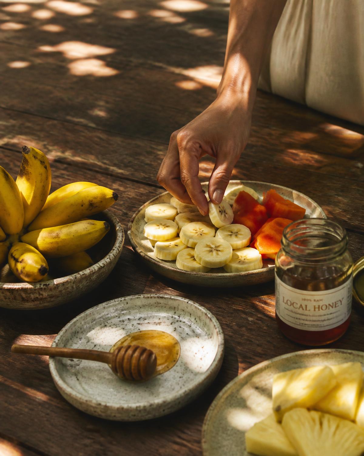 Small Canary bananas, local honey and fresh fruit on a rustic table in dappled shade